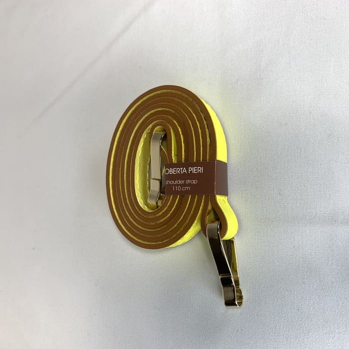 Tali bahu kuning dengan alat kelengkapan emas melingkar dan label coklat "ROBERTA PIERI shoulder strap 110 cm" dihiasi di permukaan putih.