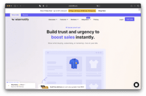 Beranda situs web Wisernotify menampilkan judul tentang membangun kepercayaan dan meningkatkan penjualan, menu navigasi di bagian atas, gambar produk kemeja biru, dan grafik toko online.